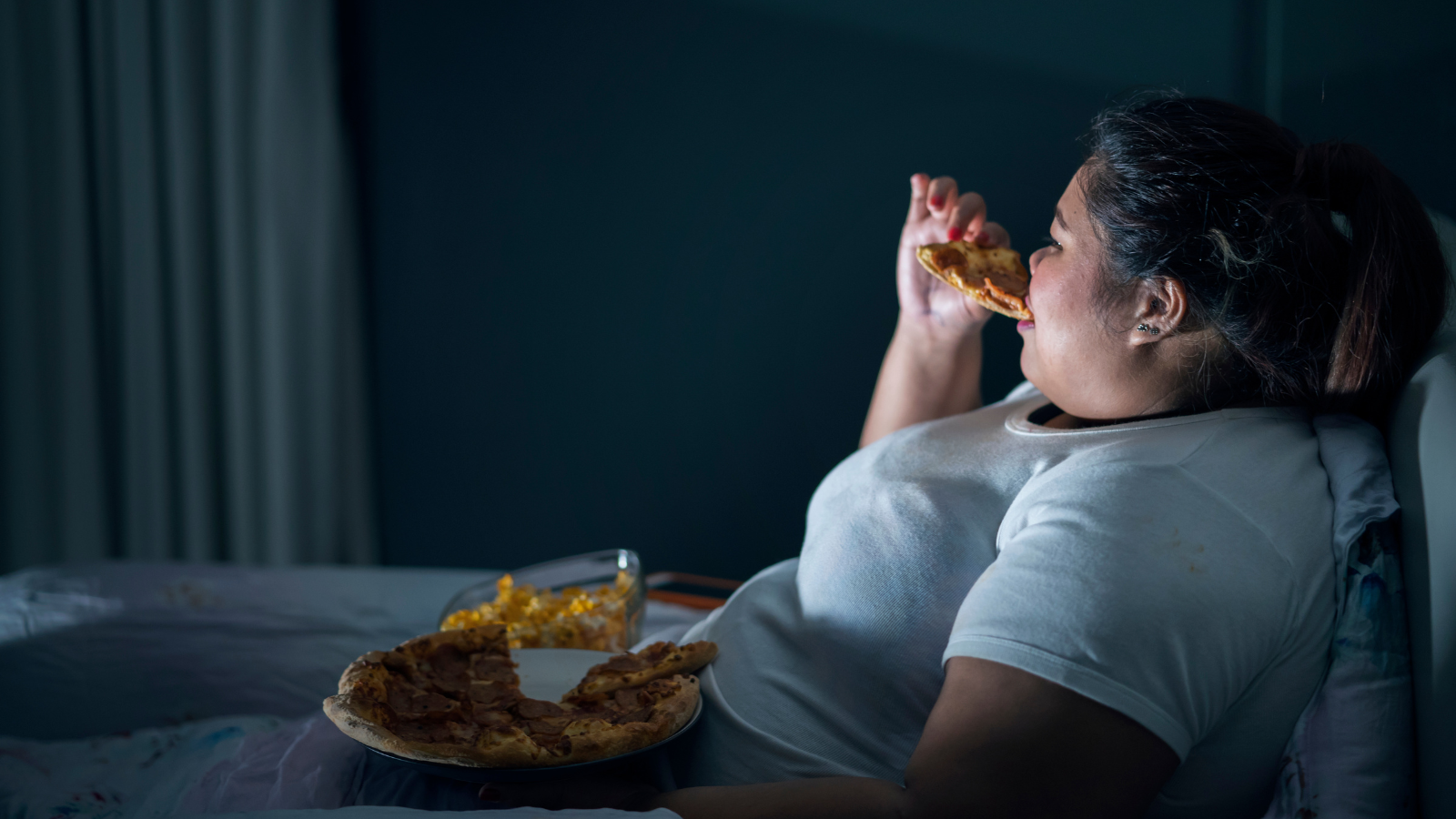 Woman eating pizza late at night in a dark room